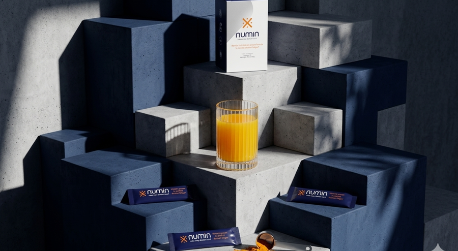 Numin supplement box and stick packs beside an orange drink on concrete blocks.