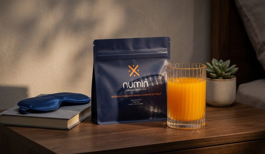 Brain supplement pouch from Numin on a bedside table beside a glass of orange tea, a sleep mask, a book, and a small succulent.