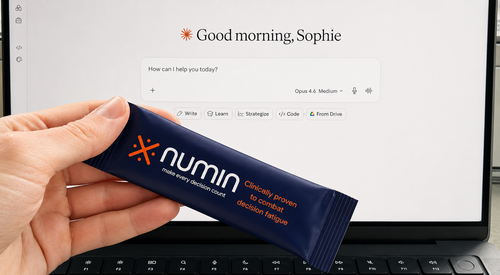 Hand holding a navy Numin nootropic stick pack in front of an AI chatbot on a laptop.