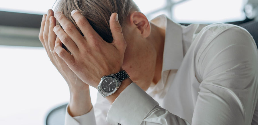Person in white shirt with hands over face, showing signs of decision exhaustion.