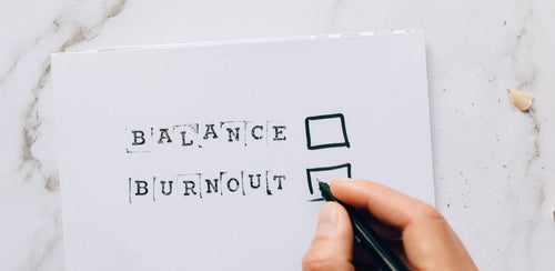 Hand with pen checking the burnout box over balance on paper, illustrating decision fatigue.