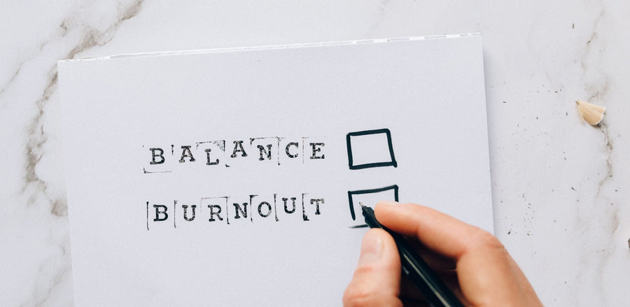 Hand with pen checking the burnout box over balance on paper, illustrating decision fatigue.