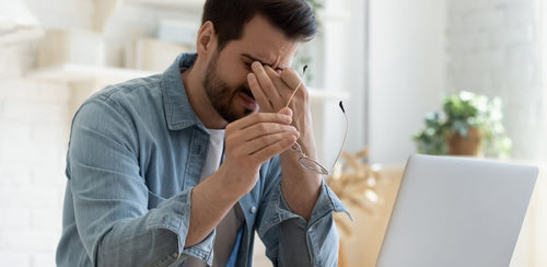 Tired person rubbing eyes and holding glasses beside a laptop, showing decision fatigue at work.