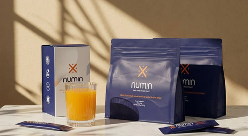 Numin decision fatigue supplement pouches and box beside a glass of prepared orange drink.