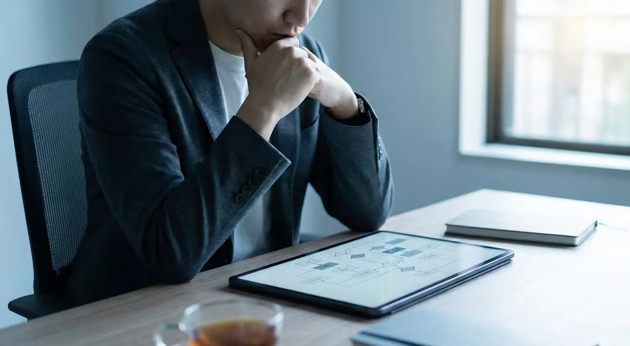 Person in blazer studies a flowchart on a tablet, weighing a plan at their desk.