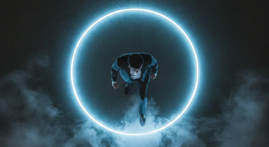Overhead view of a suited person standing inside a glowing blue neon circle amid mist.