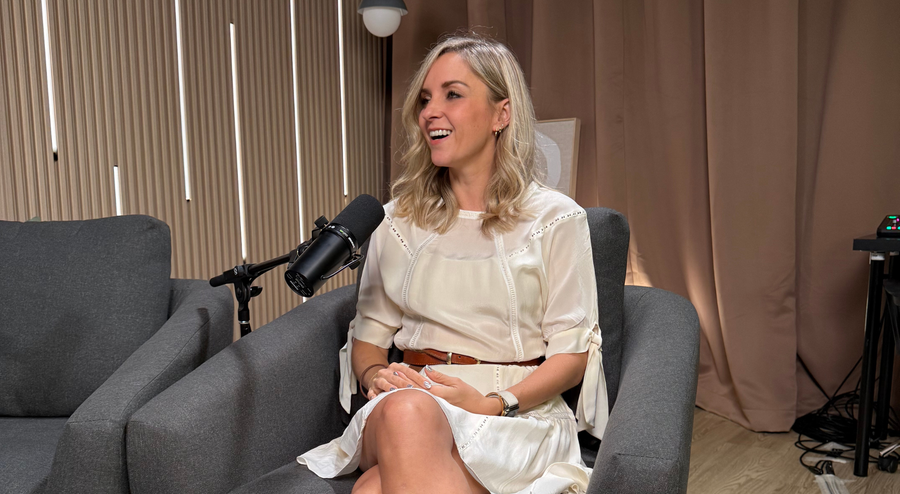 Person in cream dress speaking into a studio microphone during a podcast interview.