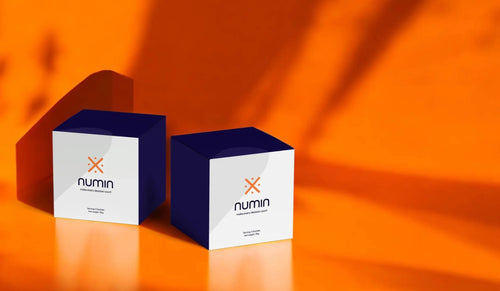 Numin packaging boxes displayed on a vibrant orange backdrop with dramatic shadow play across the surface.