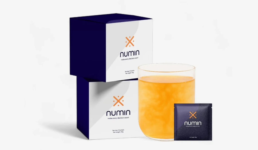 Numin nootropic drink boxes beside a glass of orange focus beverage and a sachet.