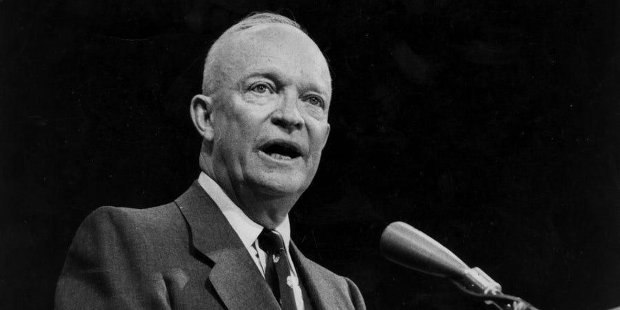 Vintage black-and-white portrait of Dwight Eisenhower speaking at a podium microphone in a suit.