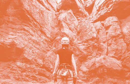 Person with backpack sitting alone in narrow orange-tinted canyon surrounded by towering rock walls