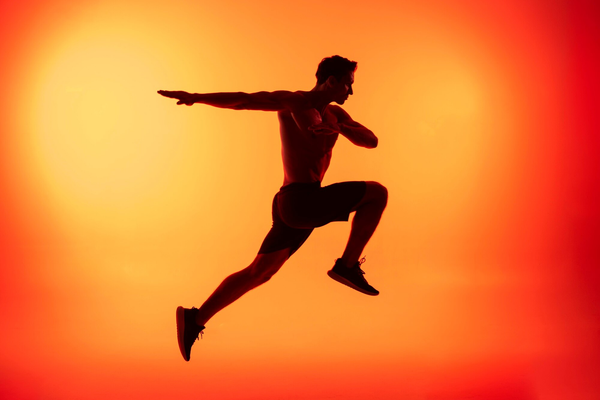 Silhouette of athletic man jumping with arms outstretched against vibrant orange sunset sky