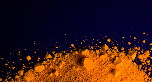 Orange brain supplement powder scattered against dark blue background with particles dispersing