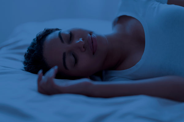 woman sleeping peacefully in bed with blue lighting, representing rest needed to combat decision fatigue