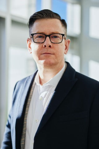 Professional podcast host in dark blazer and glasses standing in modern office setting