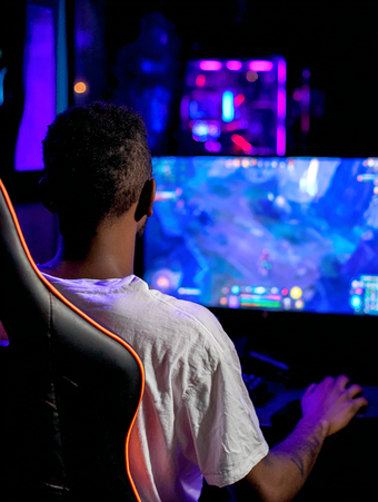 Gamer playing video games at computer setup with colorful LED lighting and multiple monitors
