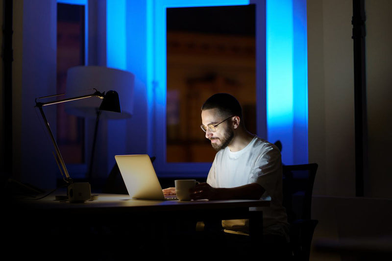 Man working late at laptop with desk lamp in blue-lit room, experiencing decision fatigue from long hours