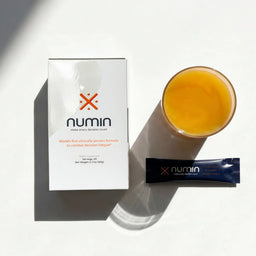 Numin 20-pack box flatlay beside a navy stick pack and glass of lemon iced tea.