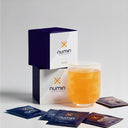 Numin brain fog supplement boxes with orange drink in glass and individual packets scattered on white surface