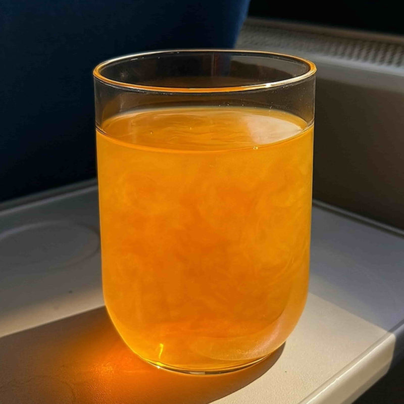 Glass of orange brain fog supplement drink on airplane tray table