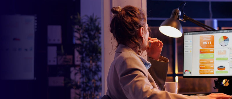 Woman experiencing decision fatigue while working late at computer with data charts and desk lamp